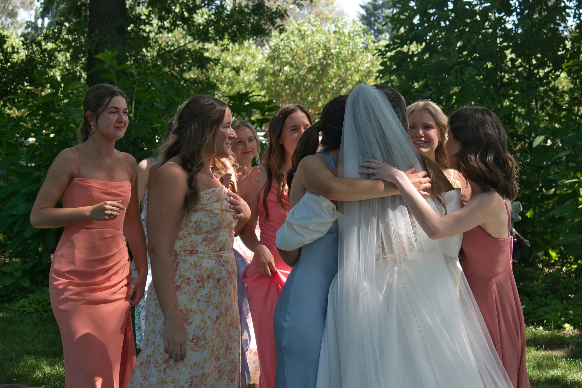 Bride hugging bridesmaids in coral dresses before wedding ceremony